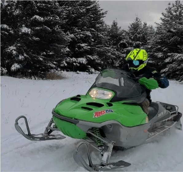 Dave Mann riding a green Arctic Cat snowmobile