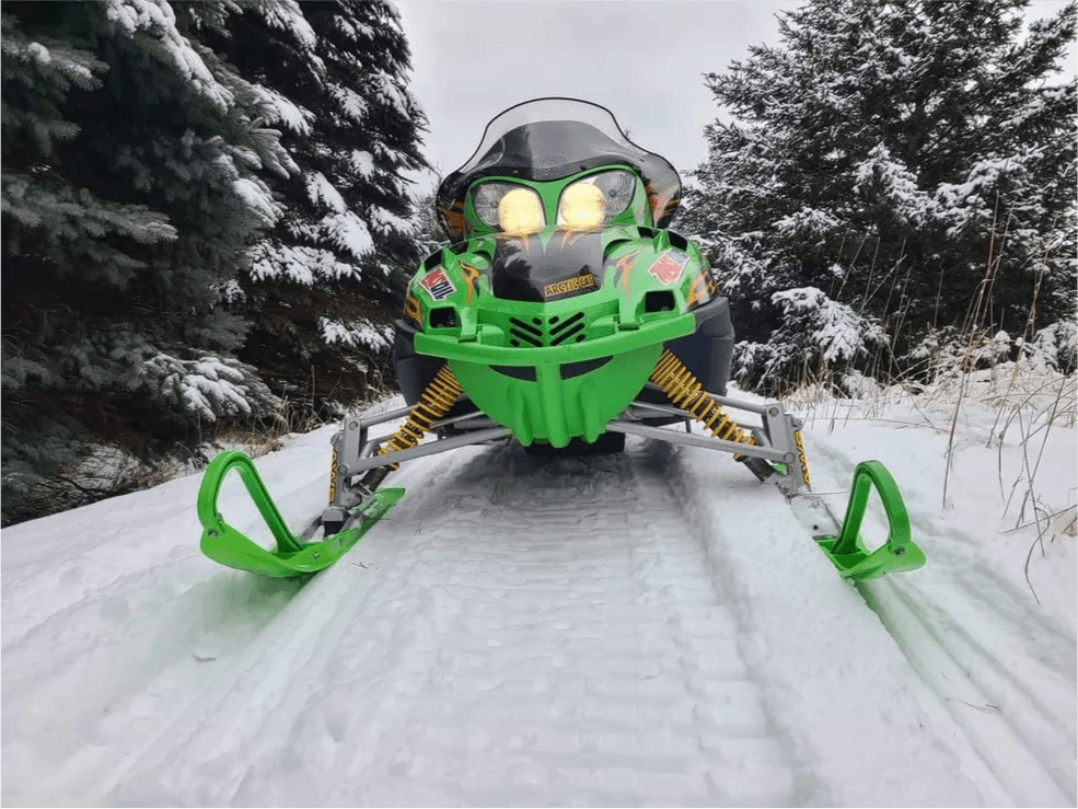Green Arctic Cat snowmobile front view on a snowy trail